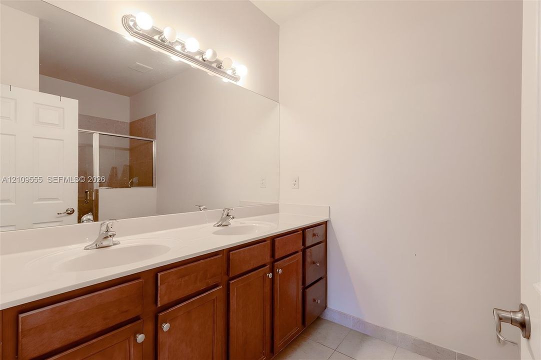 Dual-sink vanity with white countertop, wood cabinetry, large wall-mounted mirror, and multi-bulb light fixture