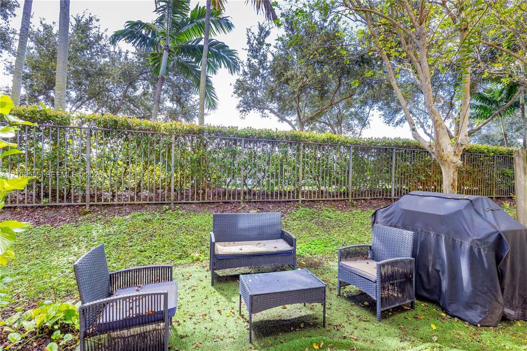 Backyard featuring a green surface, metal perimeter fencing, and mature palm and deciduous trees