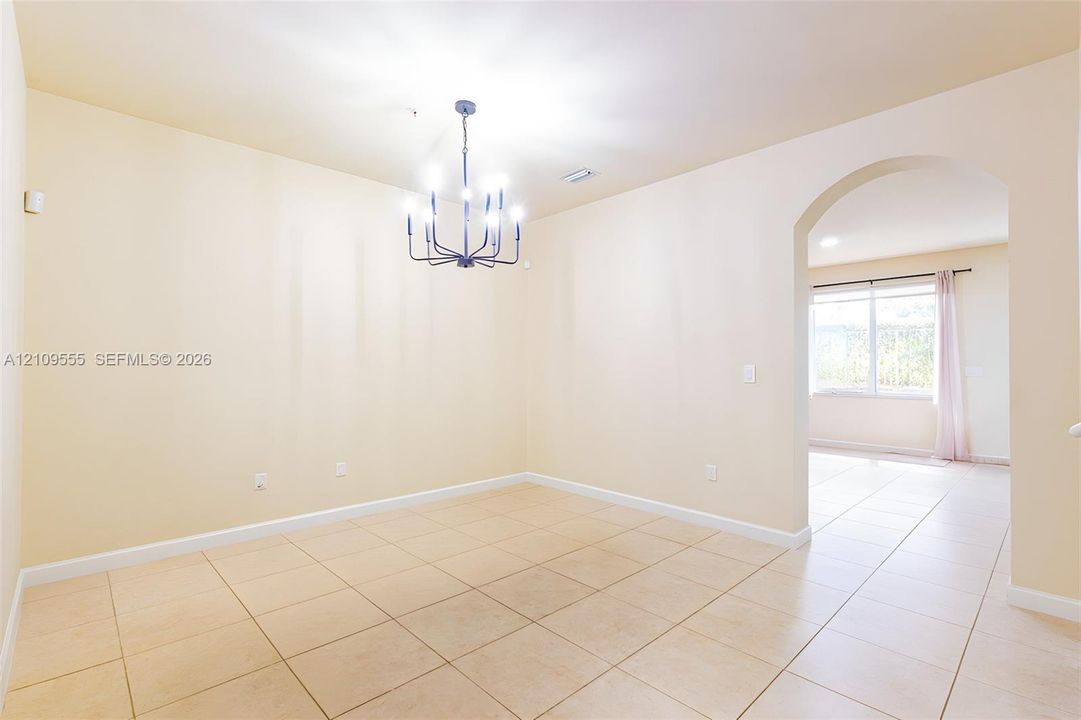 Neutral-toned interior featuring ceramic tile flooring, a geometric black metal chandelier, and a wide arched entryway