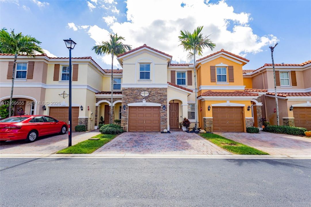 Mediterranean-style townhome featuring a stone veneer facade, terracotta roof tiles, paver driveway, and an integrated single-car garage