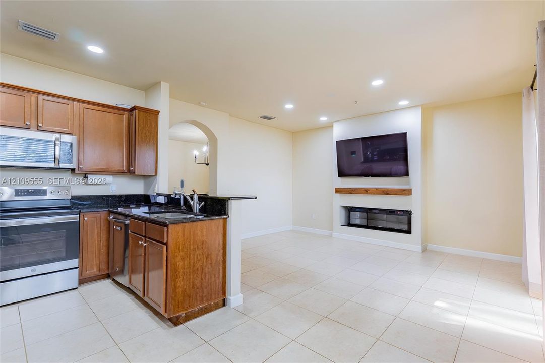 Kitchen featuring wood cabinetry, stone countertops, and stainless steel appliances, paired with a fireplace mantle and recessed lighting