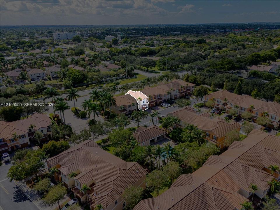 Aerial perspective of a multi-unit residential property featuring a tiled roof, stucco exterior, paved access streets, and mature landscaping within a suburban setting