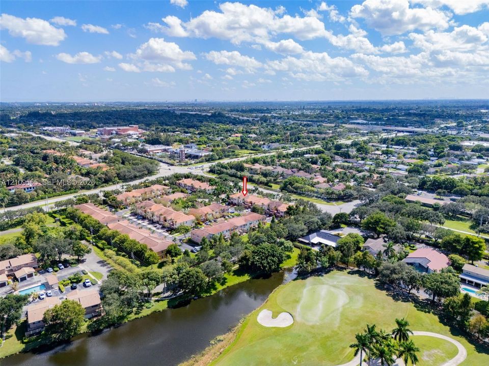 Aerial perspective featuring a multi-unit residential complex bordered by a golf course, a water feature, and mature trees