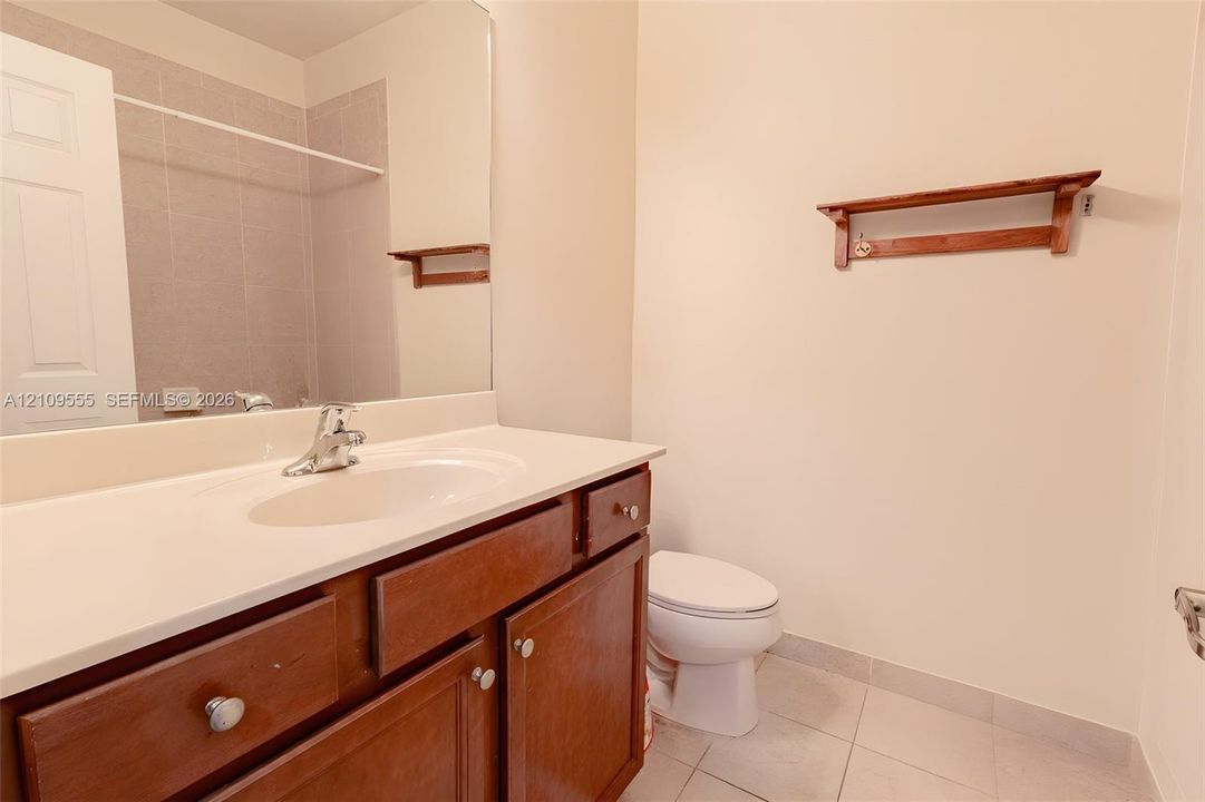 Bathroom featuring wood-finish cabinetry, a solid-surface vanity countertop with an integrated sink, a full-width mirror, and tile flooring
