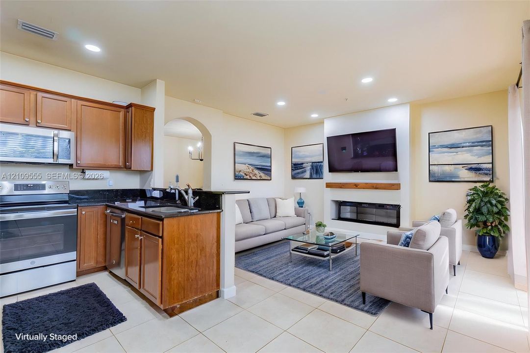 Kitchen featuring wood cabinetry, stone countertops, and stainless steel appliances, paired with a fireplace integrated into a recessed hearth with a wood mantel