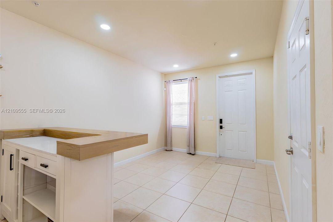 Built-in cabinetry featuring a wood-finish countertop, neutral tile flooring, recessed lighting, and a six-panel exterior entry door