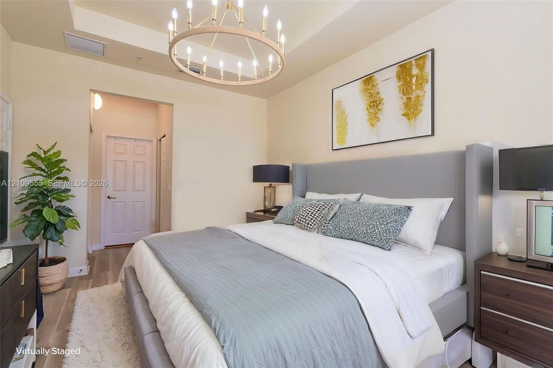 Room featuring a tray ceiling, crown molding, and a circular chandelier with brass finish, complemented by wood-finish flooring