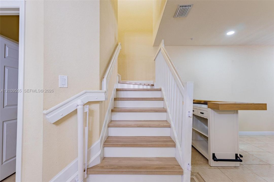 Staircase featuring wood-finish treads, white risers, and a white balustrade with a matching handrail, accompanied by a built-in cabinet with a wood-surface counter