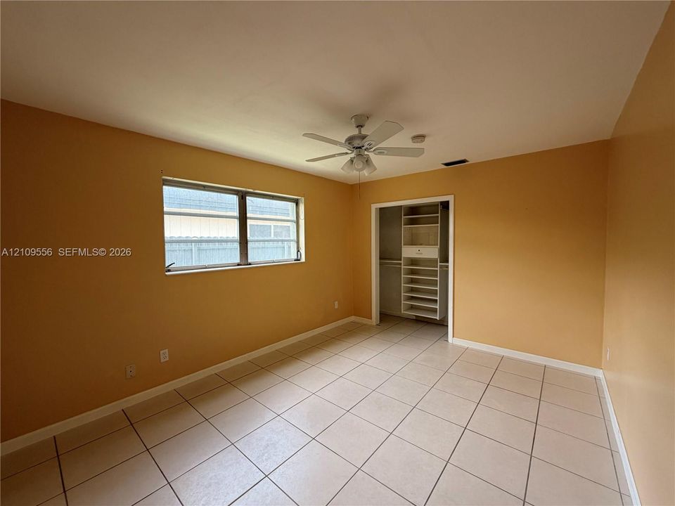 Room featuring tile flooring, multi-pane window, ceiling fan with integrated light fixture, and closet with built-in shelving