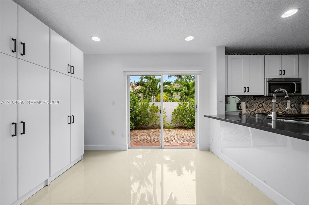 Kitchen featuring crisp white floor-to-ceiling cabinetry, dark stone countertops, patterned tile backsplash, polished neutral tile flooring, and sliding glass doors with exterior brick patio access