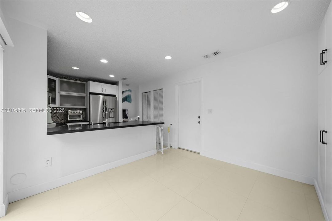 Kitchen featuring a breakfast bar with dark countertop, stainless steel refrigerator, recessed lighting, tile flooring, and floor-to-ceiling built-in cabinetry