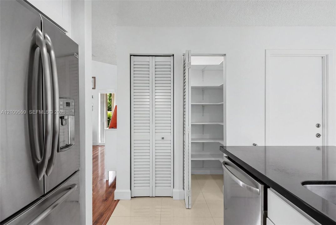 Stainless steel refrigerator, built-in pantry with white louvered doors and interior shelving, and solid-surface countertop with undermount sink