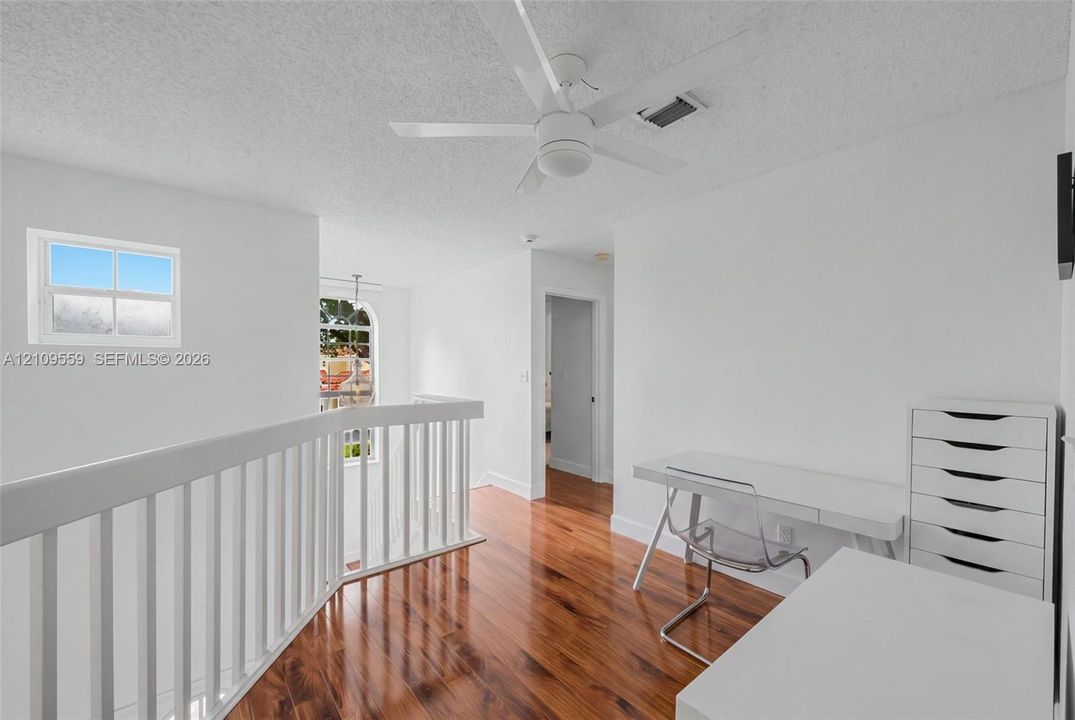 Wood-finish flooring, white wooden balustrade, arched multi-pane window, and white ceiling fan