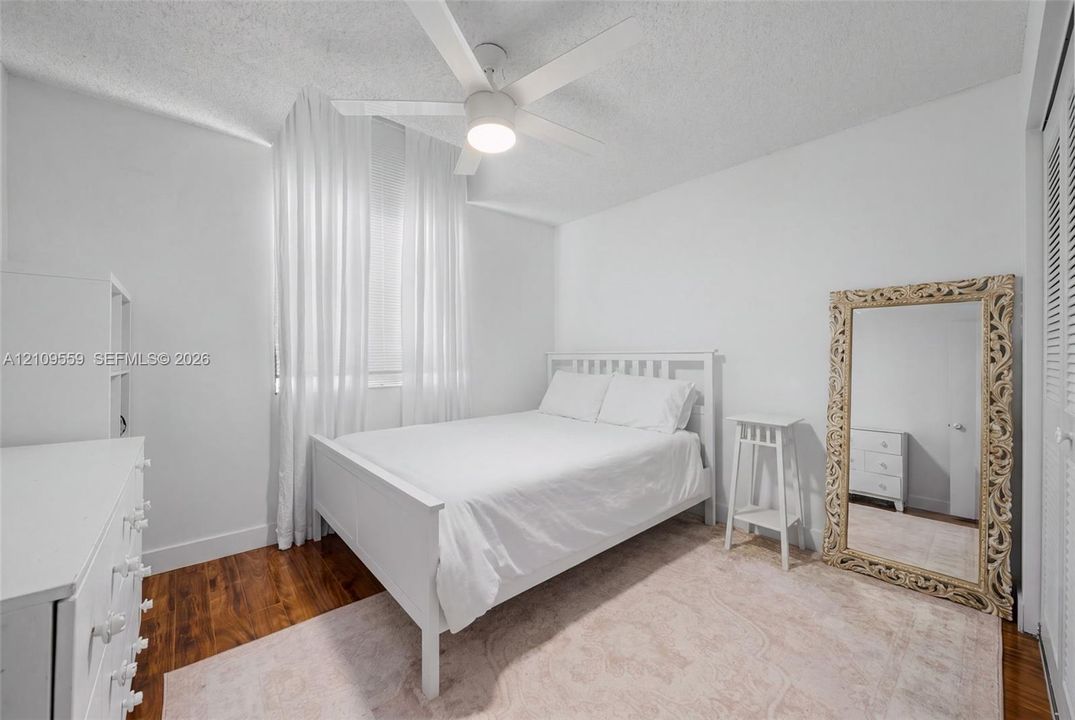 Bedroom featuring wood-finish flooring, a white ceiling fan with integrated lighting, and louvered closet doors