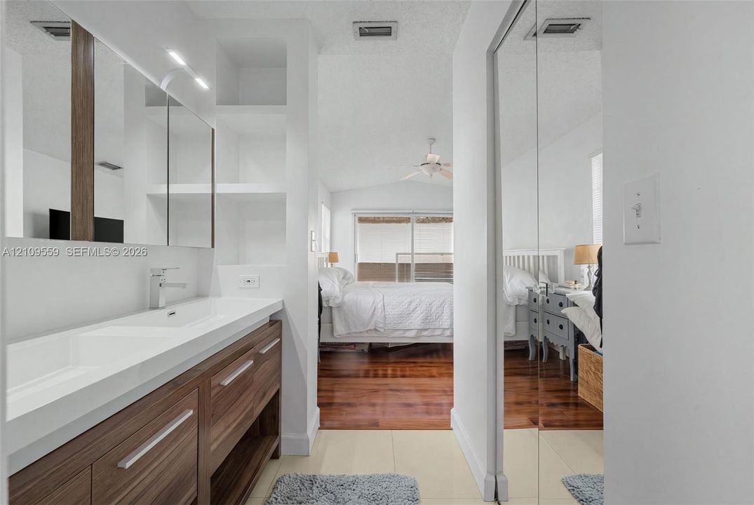 Vanity featuring a dual-sink integrated basin, wood-finish cabinetry, built-in shelving, and floor-to-ceiling mirrored closet doors