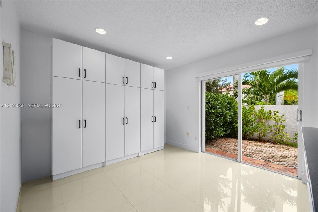 Floor-to-ceiling white cabinetry with matte black hardware, recessed lighting, and sliding glass doors opening to a brick-paved patio