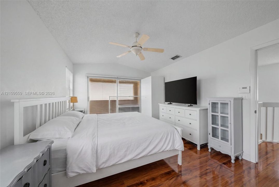 Vaulted ceiling featuring a central multi-blade ceiling fan and wood-finish flooring