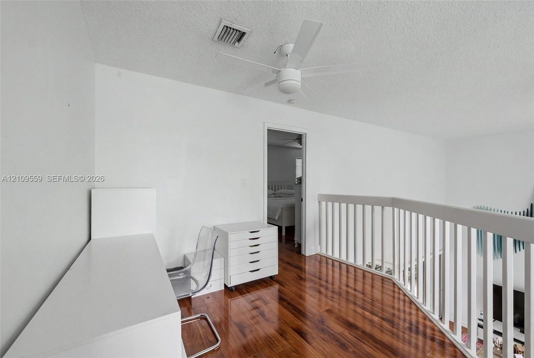 Wood-finish flooring, white spindle railing, and ceiling fan with integrated lighting