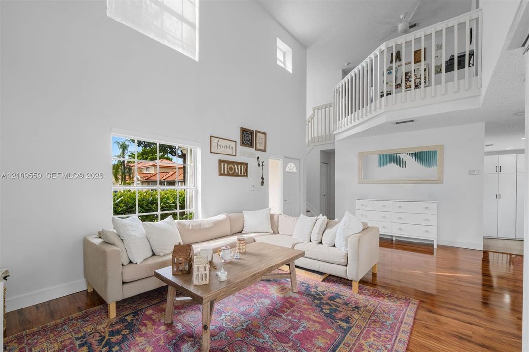 Two-story living area featuring vaulted ceilings, a prominent multi-pane window, and an interior balcony with a white railing