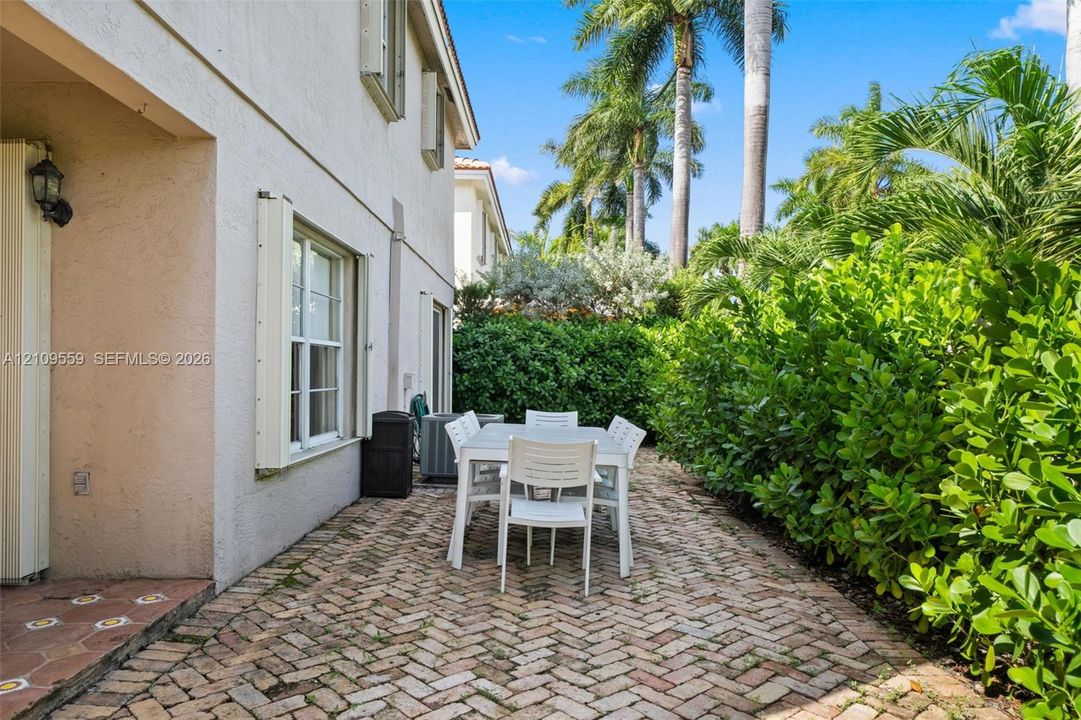 Herringbone-patterned brick paver patio featuring stucco exterior walls, multi-pane windows, and manicured perimeter hedges