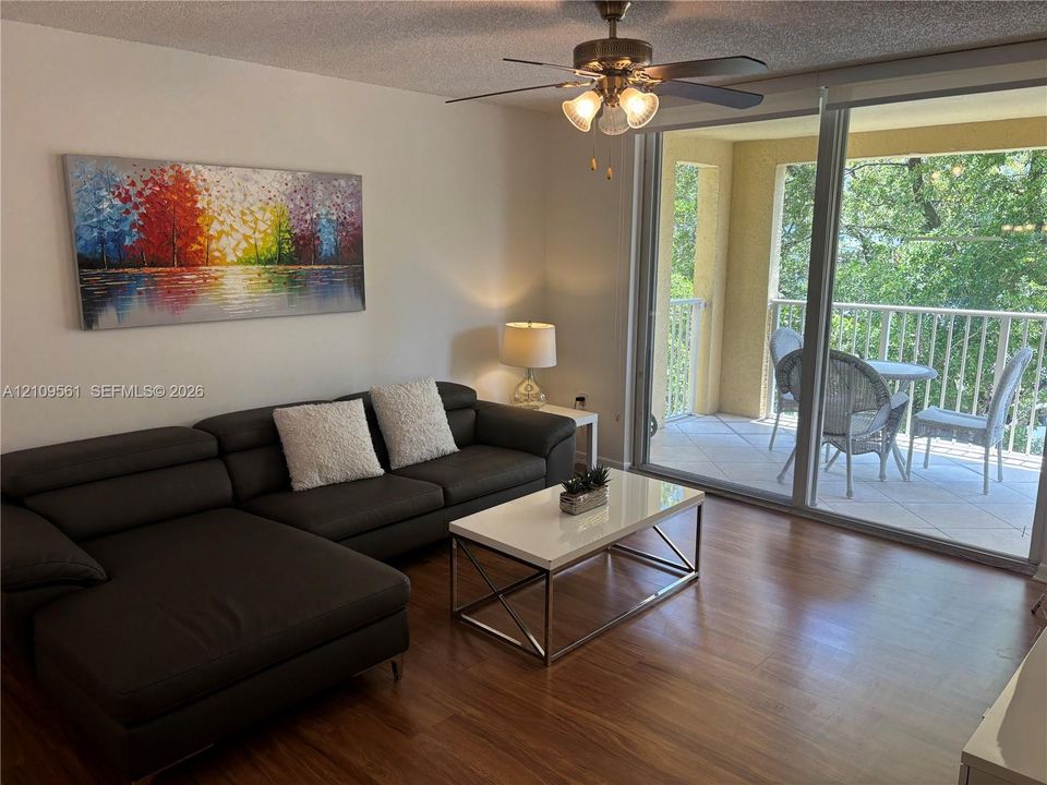 Living area featuring wood-finish flooring, a ceiling fan with integrated lighting, and a large sliding glass door providing access to a private covered balcony