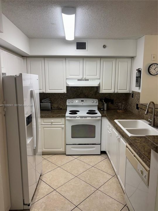 Kitchen featuring white cabinetry, stone-finish countertops, tile flooring, and white built-in appliances