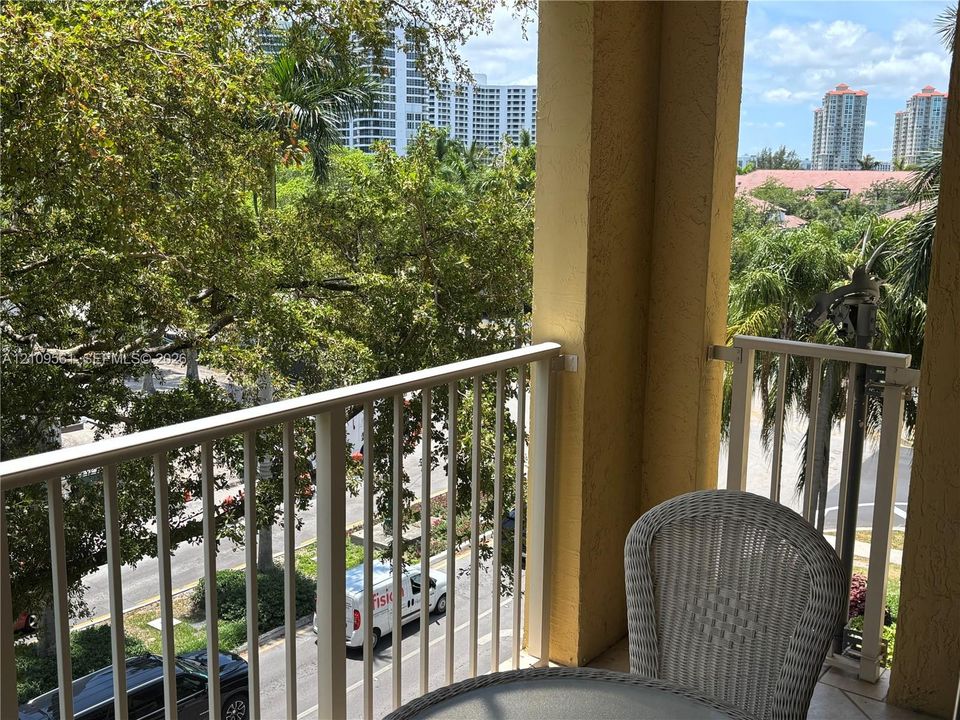 Covered balcony featuring white vertical railings, a stucco pillar, and foliage-lined exterior surroundings