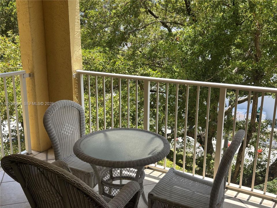 Covered balcony featuring tile flooring and metal railings, surrounded by mature trees