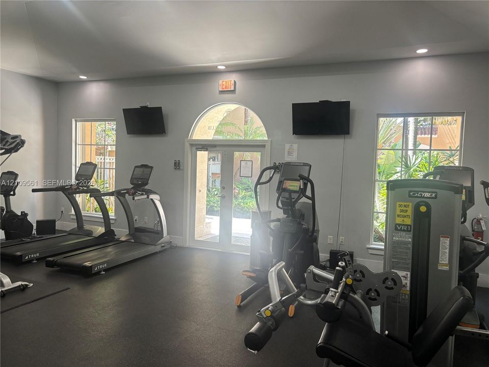Fitness area featuring rubber flooring, recessed lighting, double glass-panel entry doors with arched transom, and grid-pattern windows