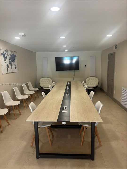 Large conference room featuring recessed lighting, neutral tile flooring, and a long built-in table with integrated power ports