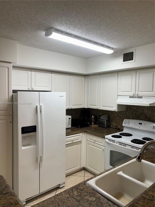 Kitchen featuring white cabinetry, stone-finish countertops, dual-basin sink, and integrated white appliances