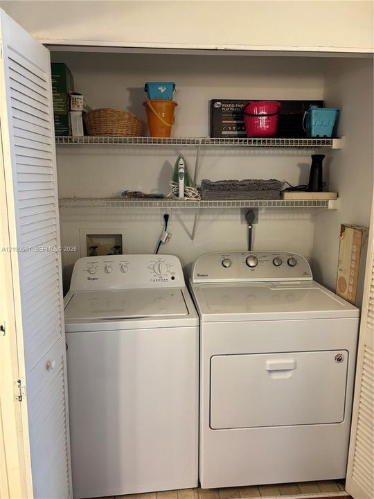 Laundry area featuring louvered bi-fold closet doors, two tiers of wire shelving, and dedicated utility hookups