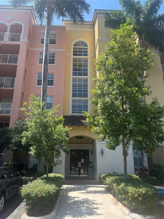 Multi-story residential building exterior featuring a stucco facade, arched window detailing, covered entryway, and integrated private balconies