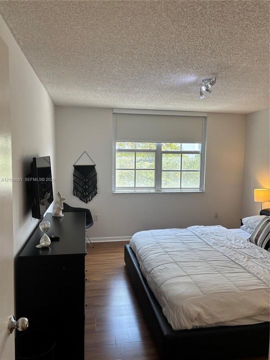 Room featuring wood-finish flooring, a multi-pane window with a roller shade, and ceiling-mounted track lighting