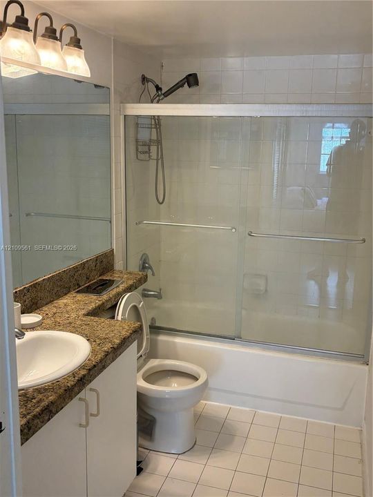 Bathroom featuring a stone-finish countertop, white cabinetry, a full-width vanity mirror, a tub-shower combination with sliding glass doors, and tiled flooring