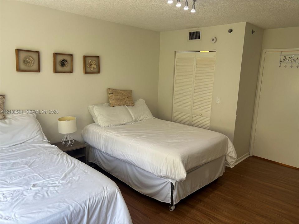 Room featuring wood-finish flooring, white louvered closet doors, and multi-bulb ceiling lighting