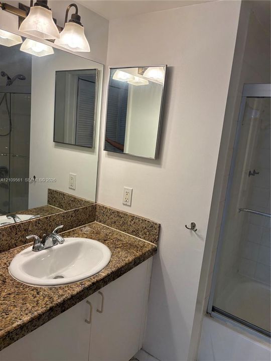 Vanity featuring a stone-composite countertop, integrated oval basin, three-light polished metal fixture, large wall-mounted mirror, and a glass-enclosed shower stall