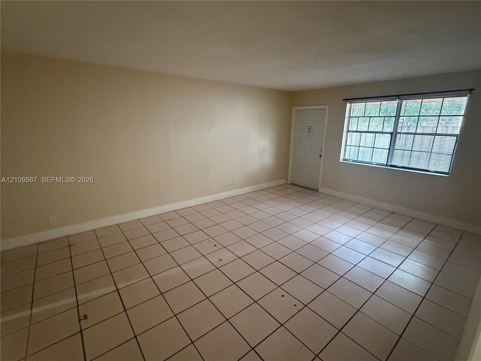 Neutral-toned interior space featuring light-colored tile flooring, smooth walls, and a window with a colonial grille pattern