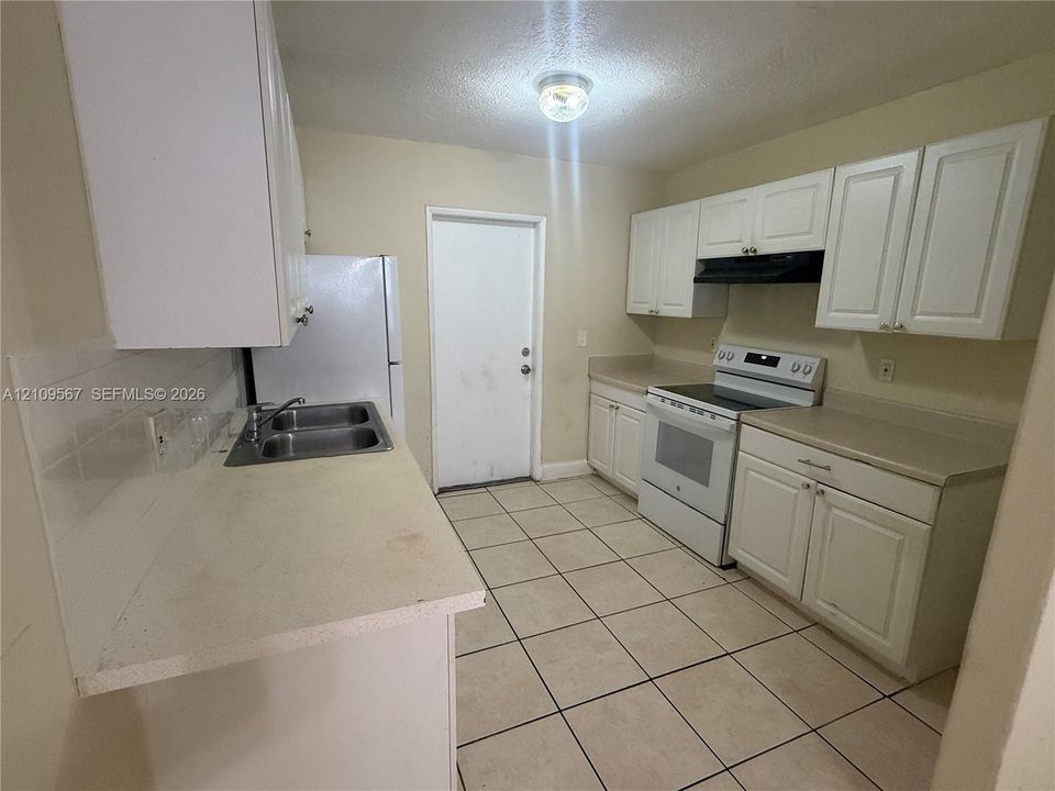 Kitchen featuring white cabinetry, solid surface countertops, stainless steel dual-basin sink, tile flooring, and integrated range hood