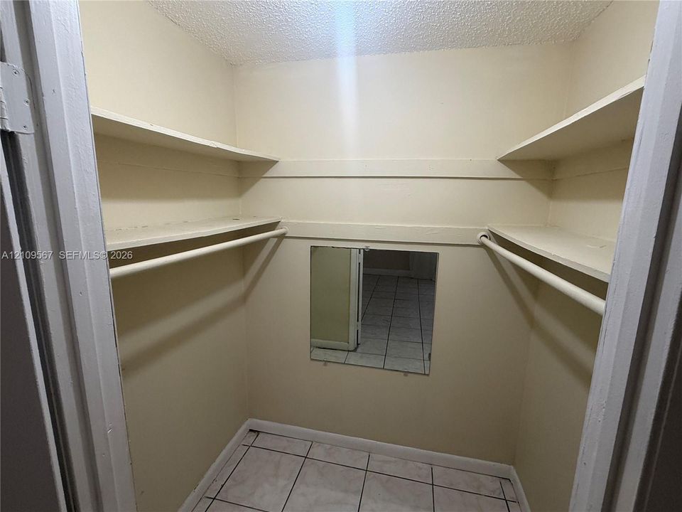 Walk-in storage space featuring multi-level shelving, integrated hanging rods, square tile flooring, and a wall-mounted mirror