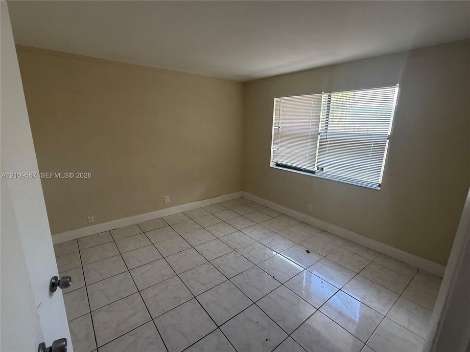 Room featuring large-format ceramic tile flooring and multi-pane window with horizontal blinds