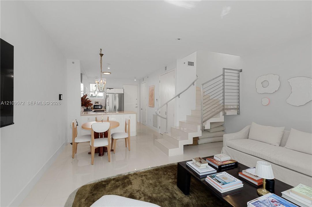 Open-concept interior featuring light-toned flooring, a stainless steel refrigerator, and a staircase with a horizontal metal railing system