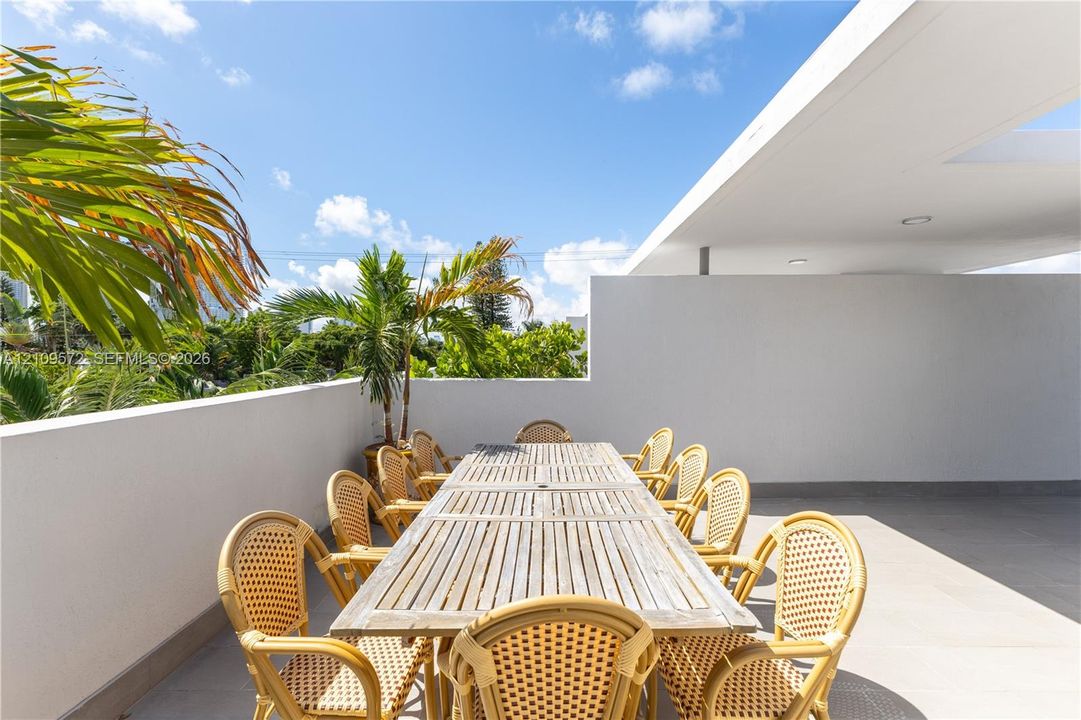 Open-air rooftop terrace featuring large-format tile flooring, a partial roof overhang, and solid perimeter walls