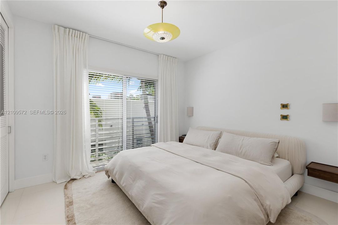 Sliding glass doors with horizontal blinds, neutral wall-to-wall stone flooring, recessed lighting, and dual wall-mounted light fixtures