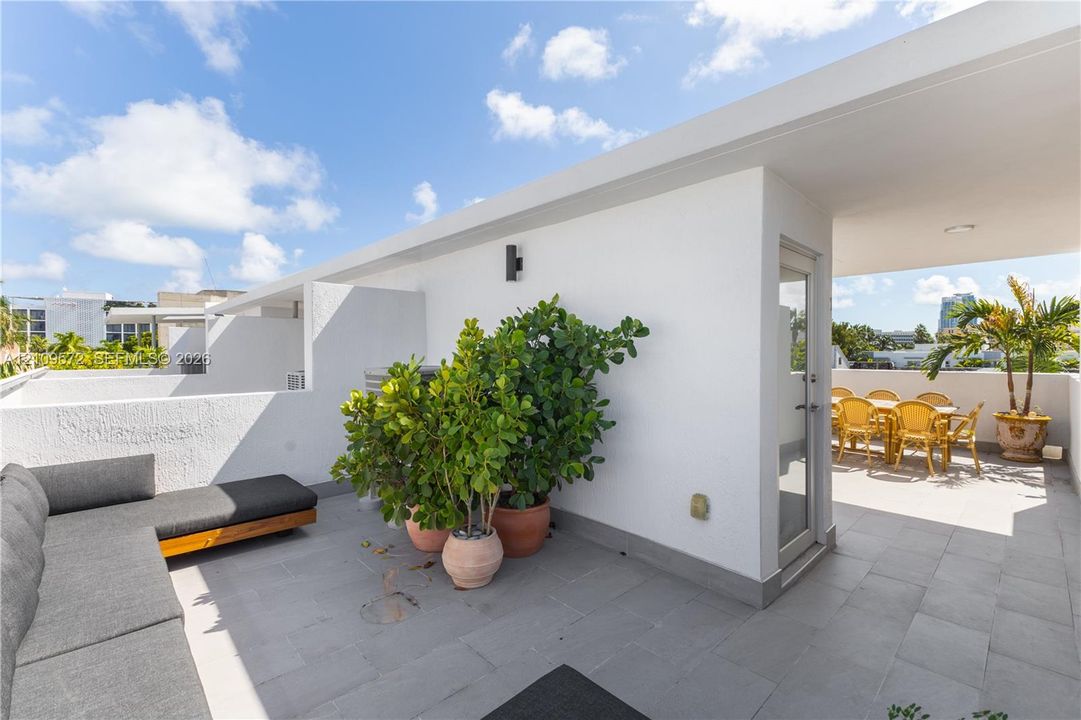Covered rooftop terrace featuring light-grey tile flooring, white stucco walls, and a glass-paneled exterior door