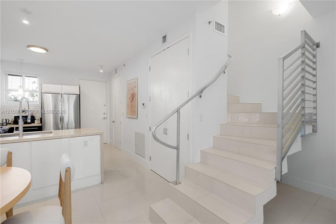 Modern interior featuring tile flooring throughout, a kitchen island with stone-finish countertops, stainless steel appliances, and a staircase with metal railings