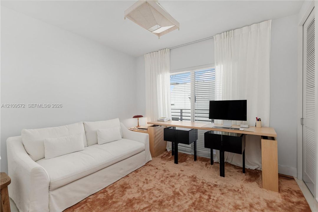 Bright room featuring a flush-mount geometric ceiling light, windowed wall with slider access to an exterior balcony, and a louvered closet door