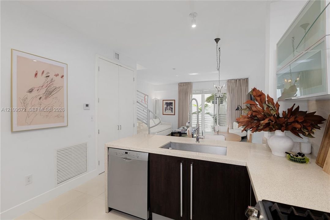 Kitchen featuring stone-finish countertops, stainless steel undermount sink with a gooseneck faucet, stainless steel dishwasher, dark wood-finish cabinetry, and upper cabinetry with frosted glass inserts