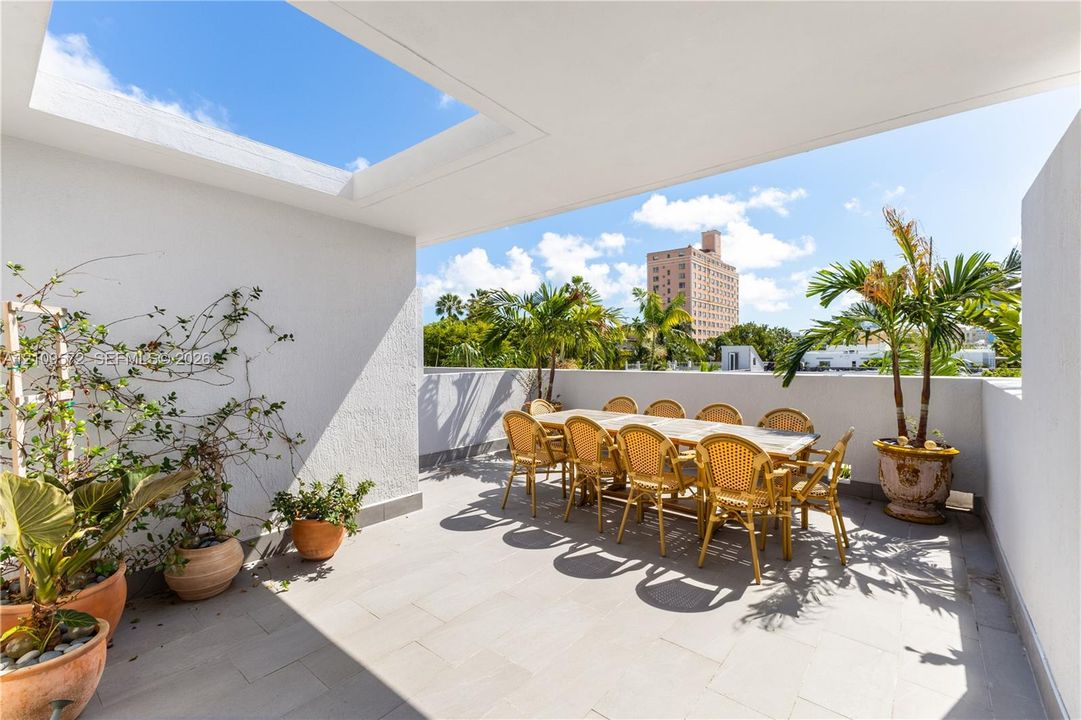 Outdoor terrace featuring stone-tile flooring, a recessed ceiling cut-out, solid stucco wall perimeter, and built-in trellis