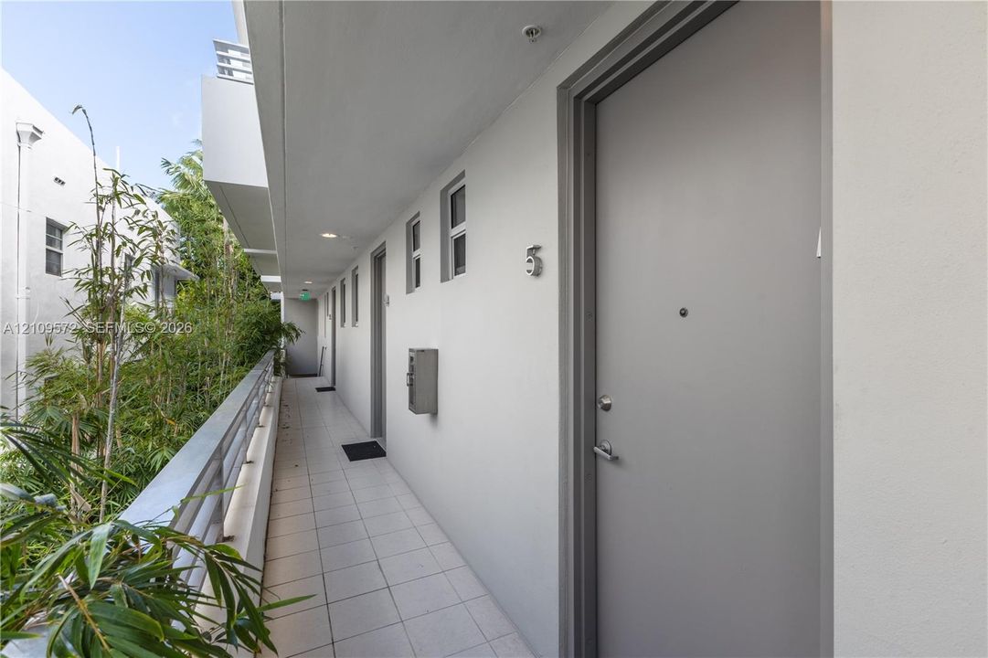 Exterior corridor featuring smooth-finish light-toned walls, tile flooring, metal handrail, and wall-mounted metal mailboxes